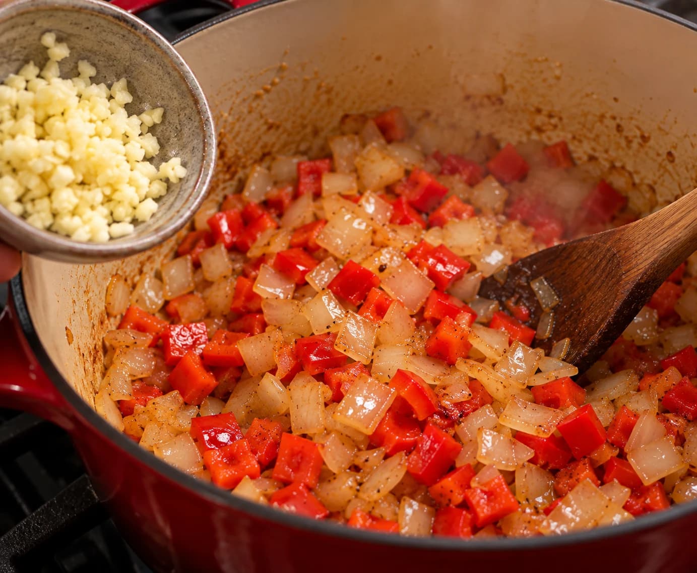 Chopped garlic being added to sautéed onions and red bell peppers