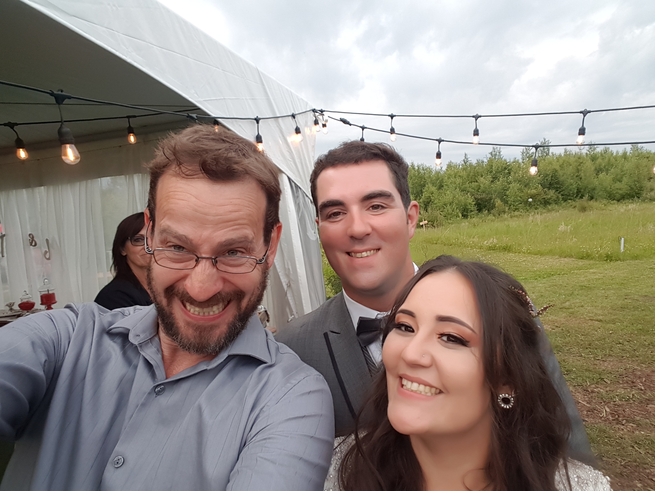 Greg taking a selfie with a wedding couple outside the reception tent
