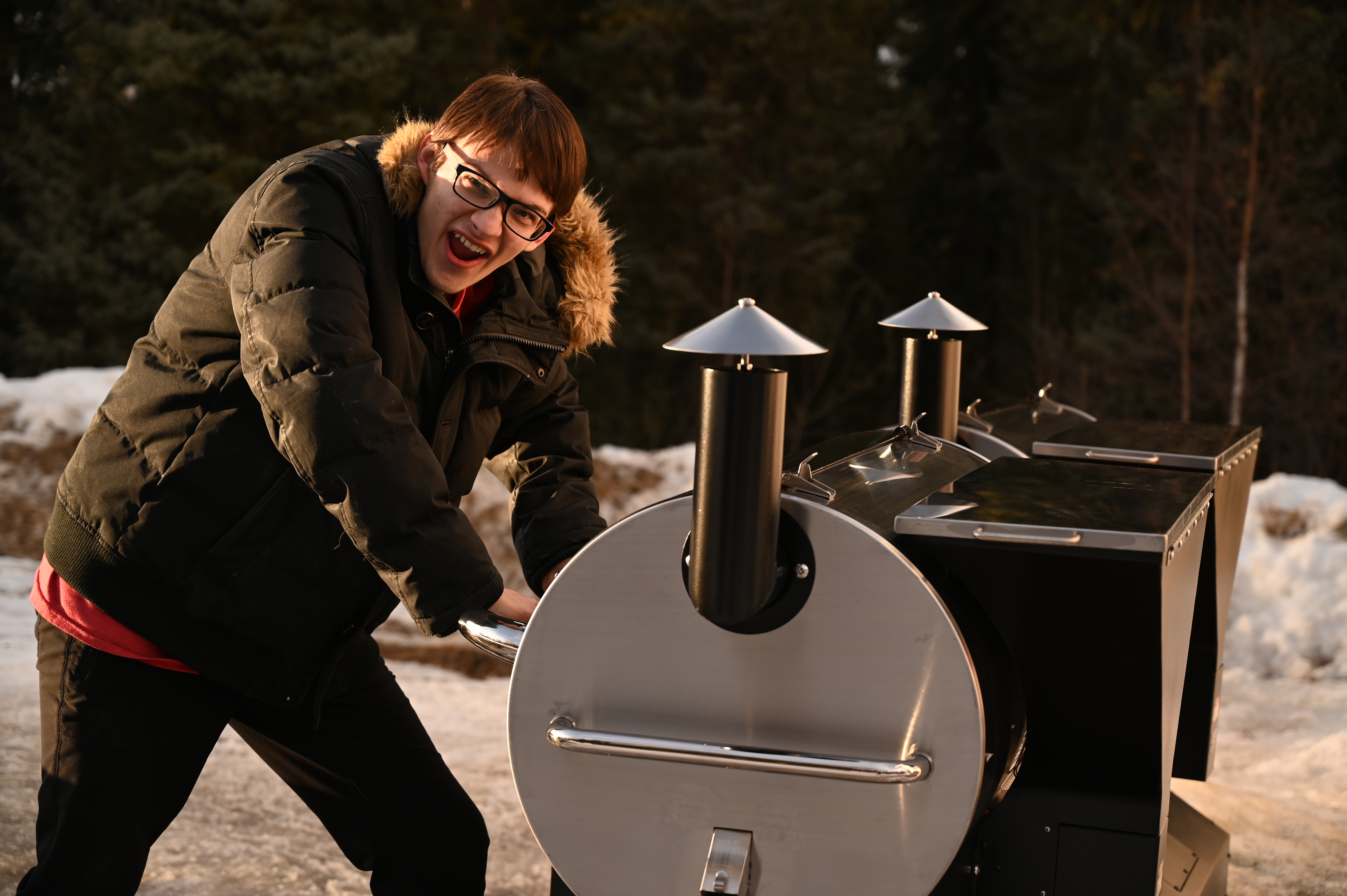 A young helper smiling beside a couple of Back Forty Barbeque mobile smokers