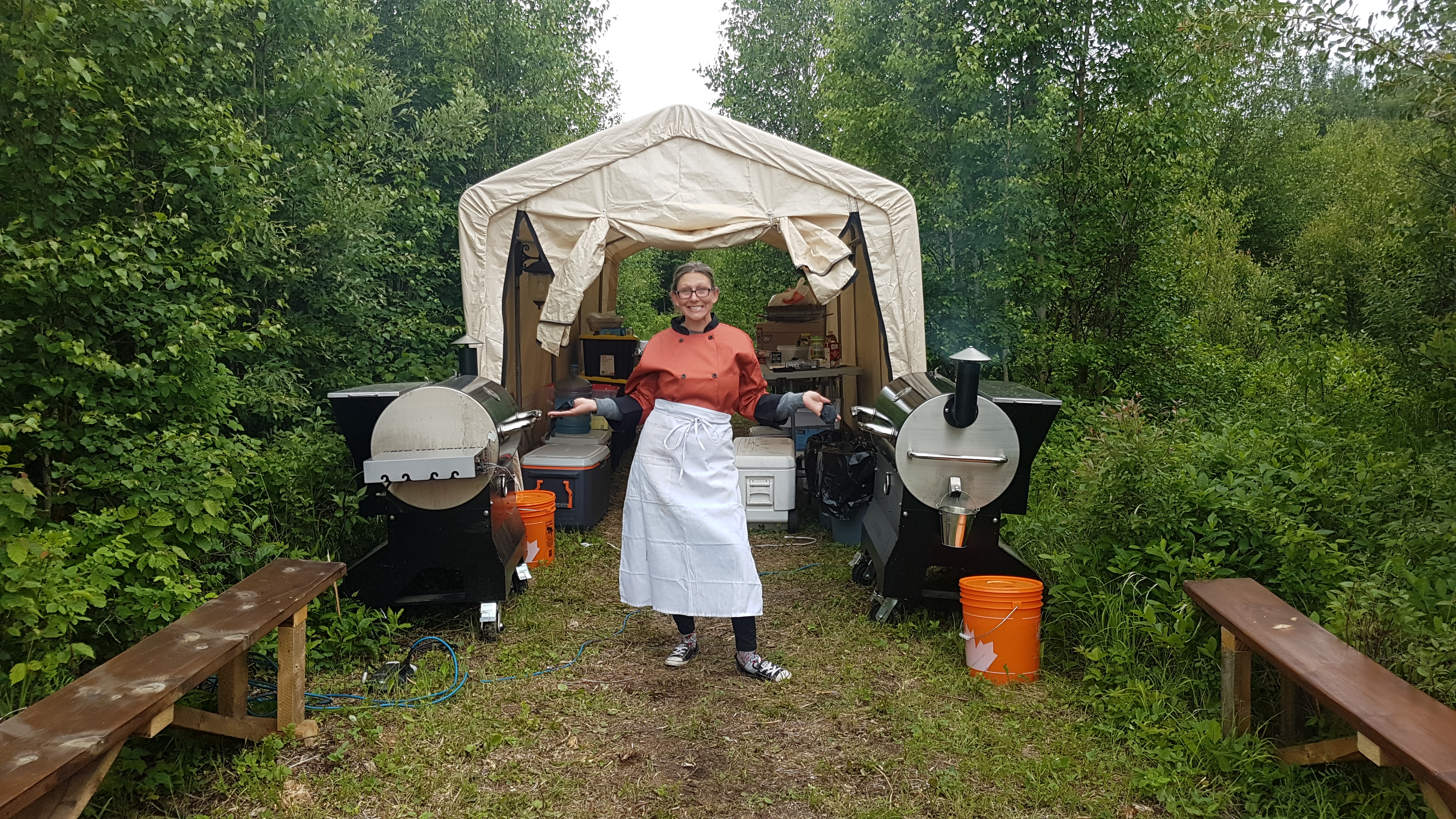 Michelle standing between two mobile smokers at an outdoor Back Forty Barbeque setup