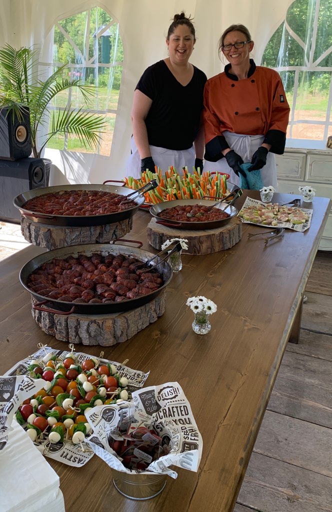 Michelle and Jenn behind a table with a paella pan and smoked chicken bites